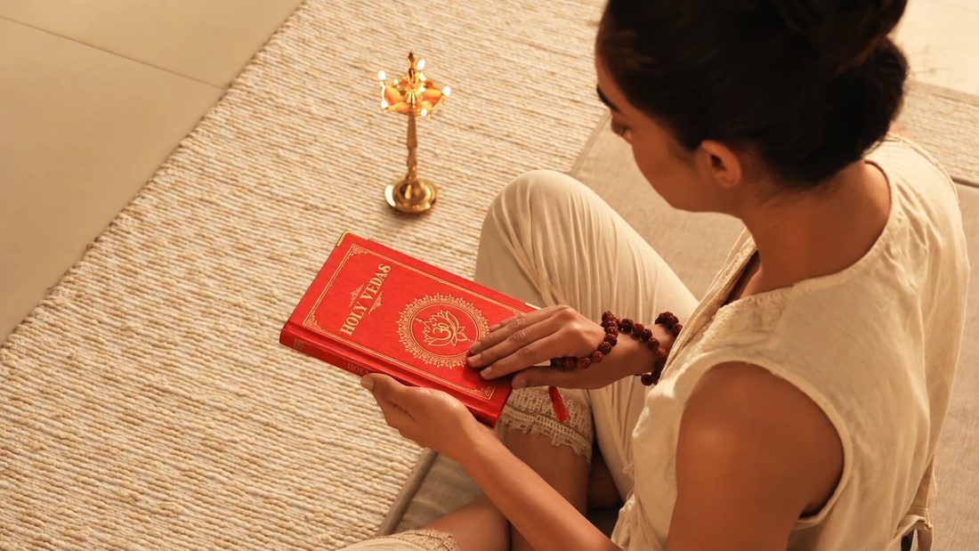 Mulher sentada numa esteira de palha a ler um livro vermelho dos Vedas sagrados junto a uma lamparina de latão, para Art of Vedas